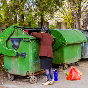 Homeless woman is searching for food in garbage dumpster. Woman in poverty is searching something in container.